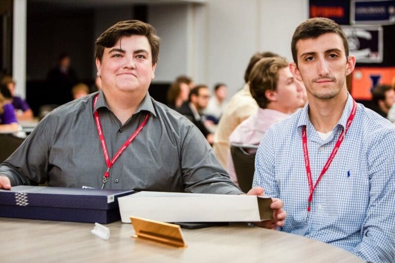Two men at a conference table with awards.