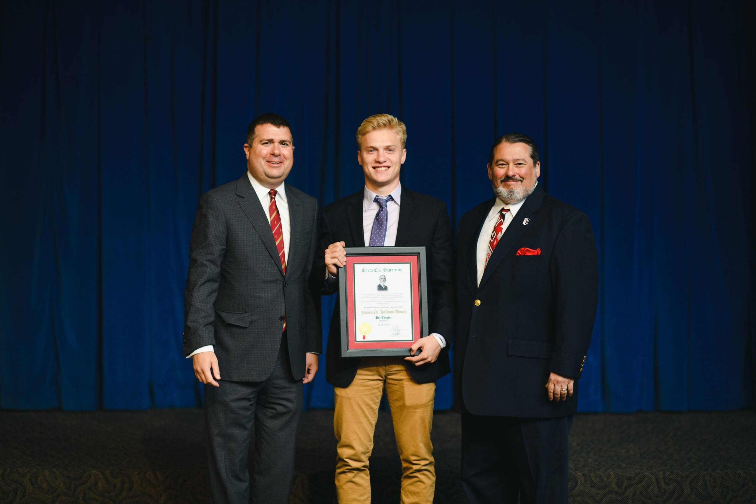 2018/2019 Holland Award - Winner Three men celebrating an award ceremony on stage.