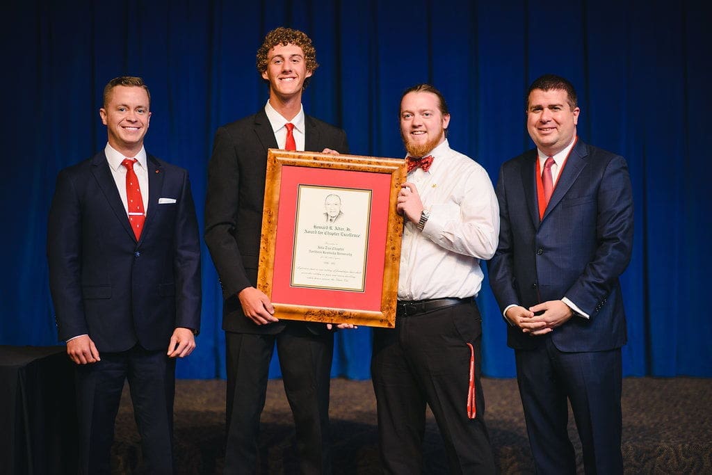 Award ceremony with four men holding a framed certificate.