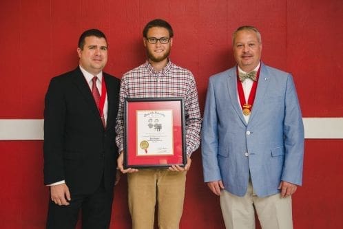 Three men posing with an award certificate.