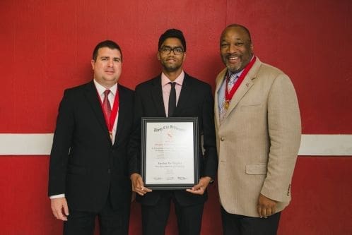 Three men posing with an award certificate.