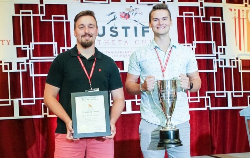 Two men holding award plaque and trophy at event.