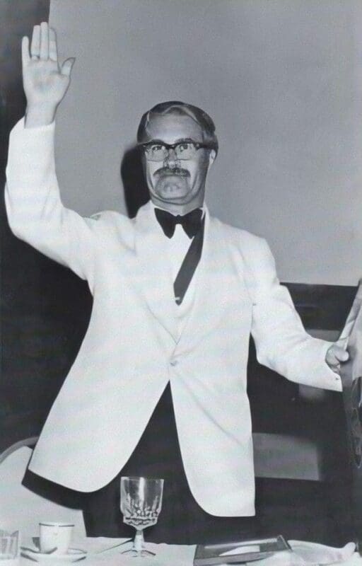 Man in white tuxedo conducting an orchestra.