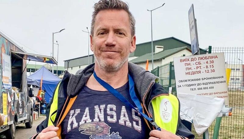 Man wearing Kansas shirt at outdoor event.