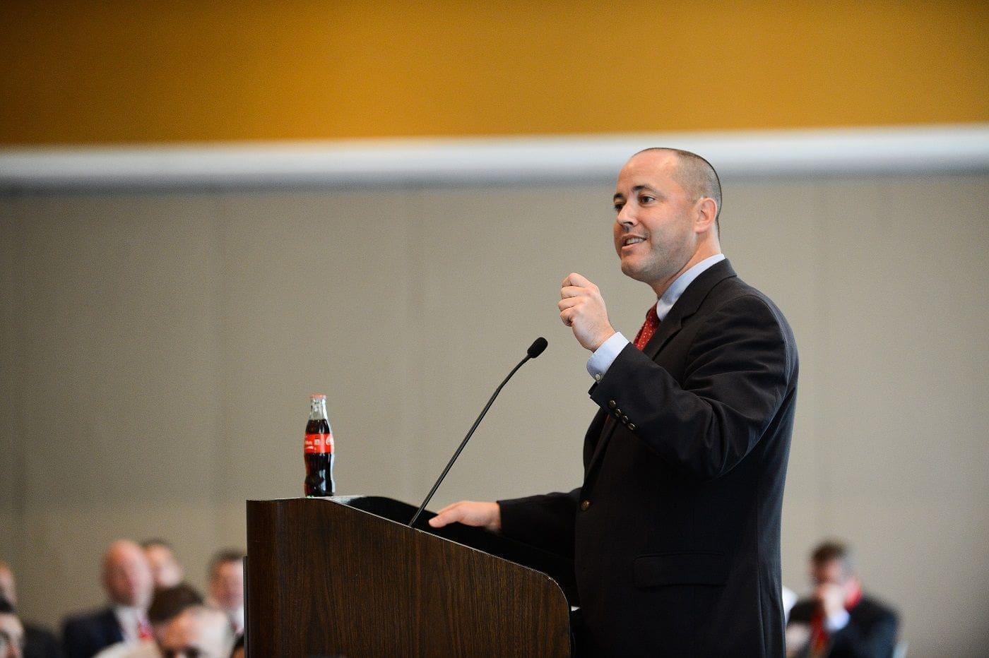 Man speaking at podium with Coca-Cola bottle.