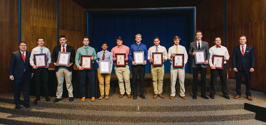 Young men holding awards on stage at ceremony.