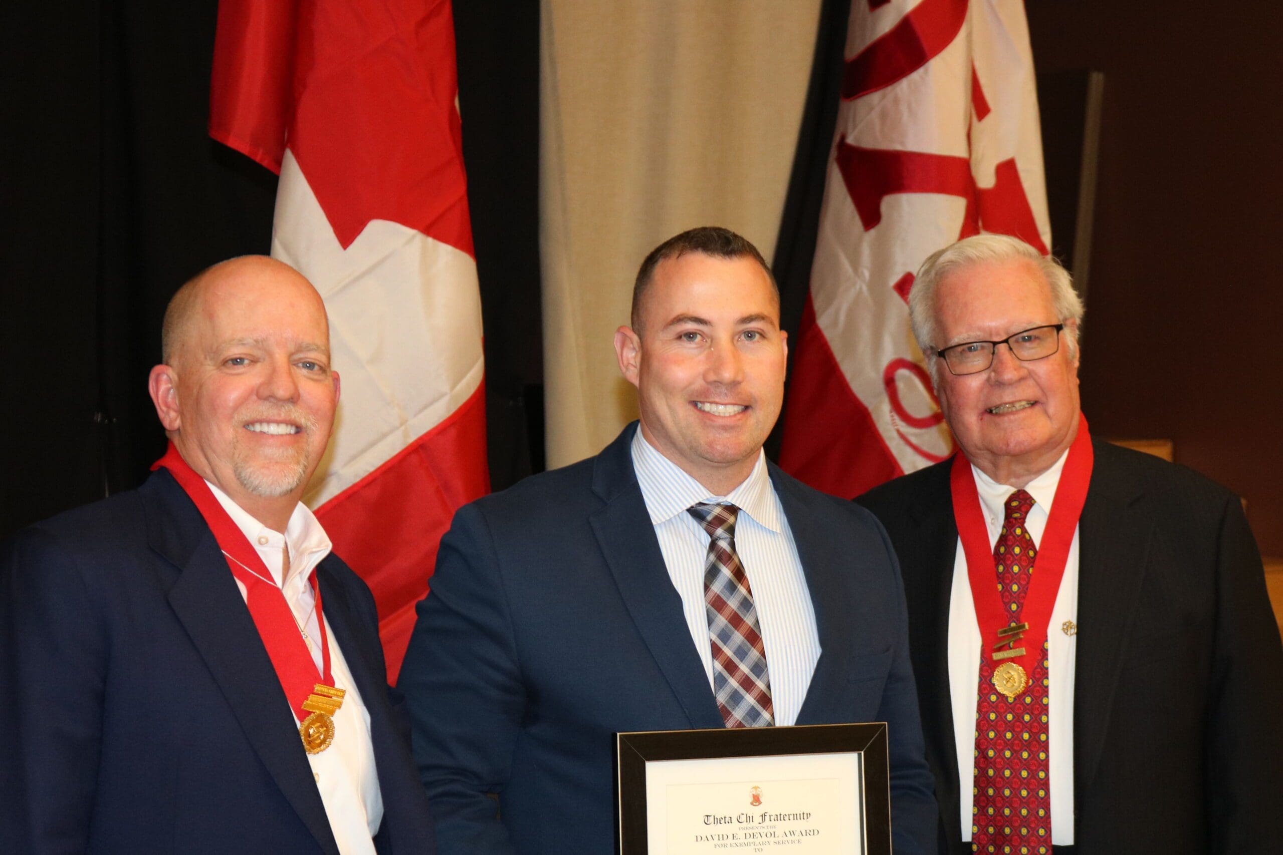 Three men holding an award, Canadian flags in background.