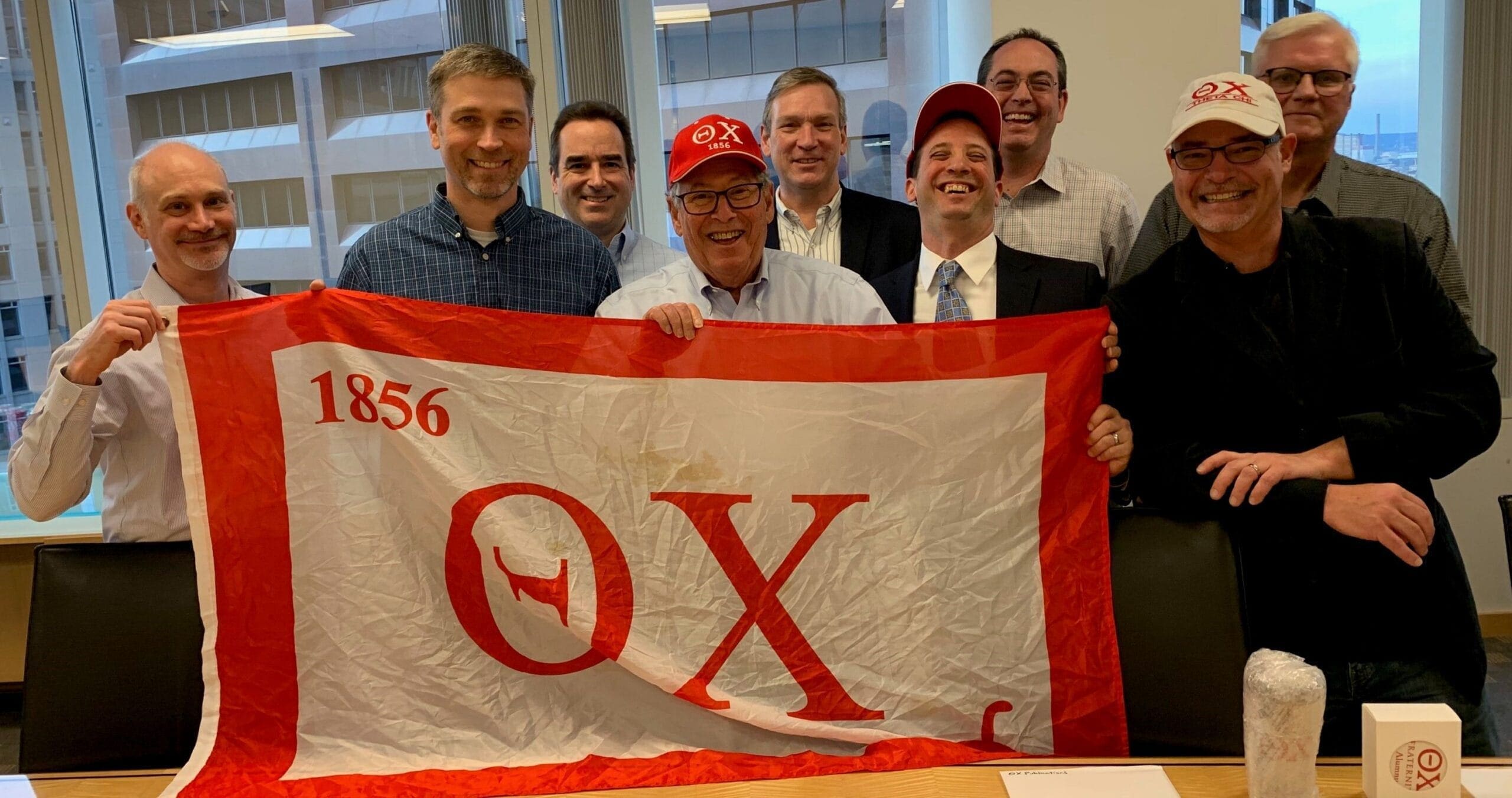 Group of men holding a fraternity flag and smiling.