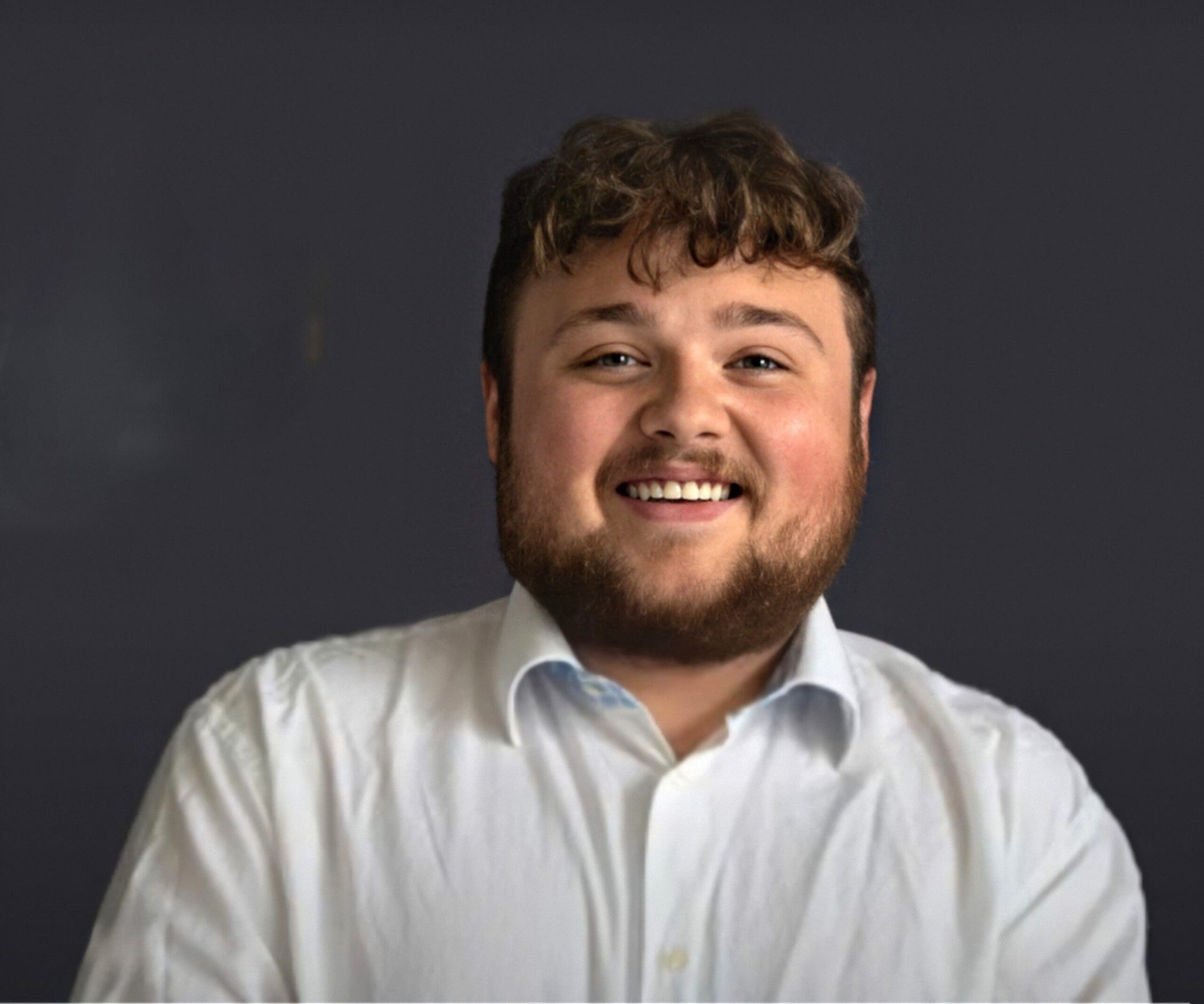 Smiling man in a white shirt against dark background.