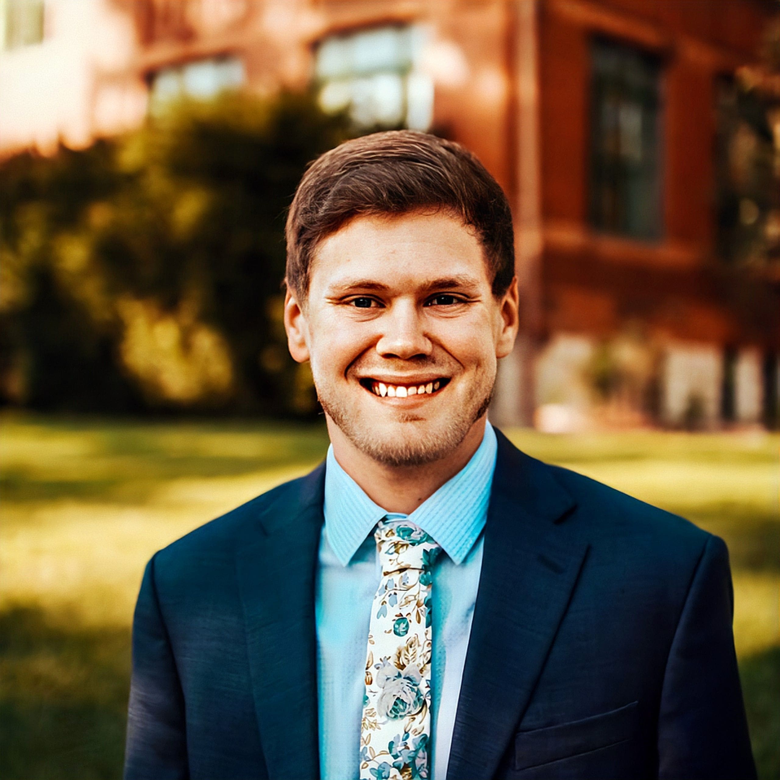 Hunter Smith Smiling man in suit outdoors with greenery background.