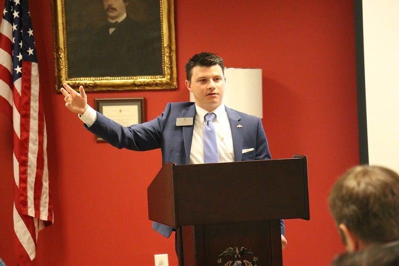 Man speaking at podium in formal setting.