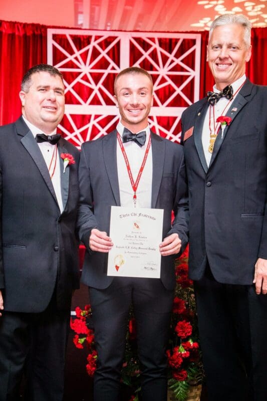 Three men in tuxedos holding an award certificate.