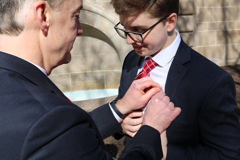 Man adjusting a young man's tie outdoors.