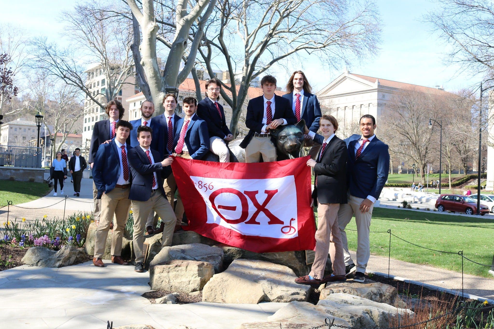 Group of students posing with fraternity flag outdoors.