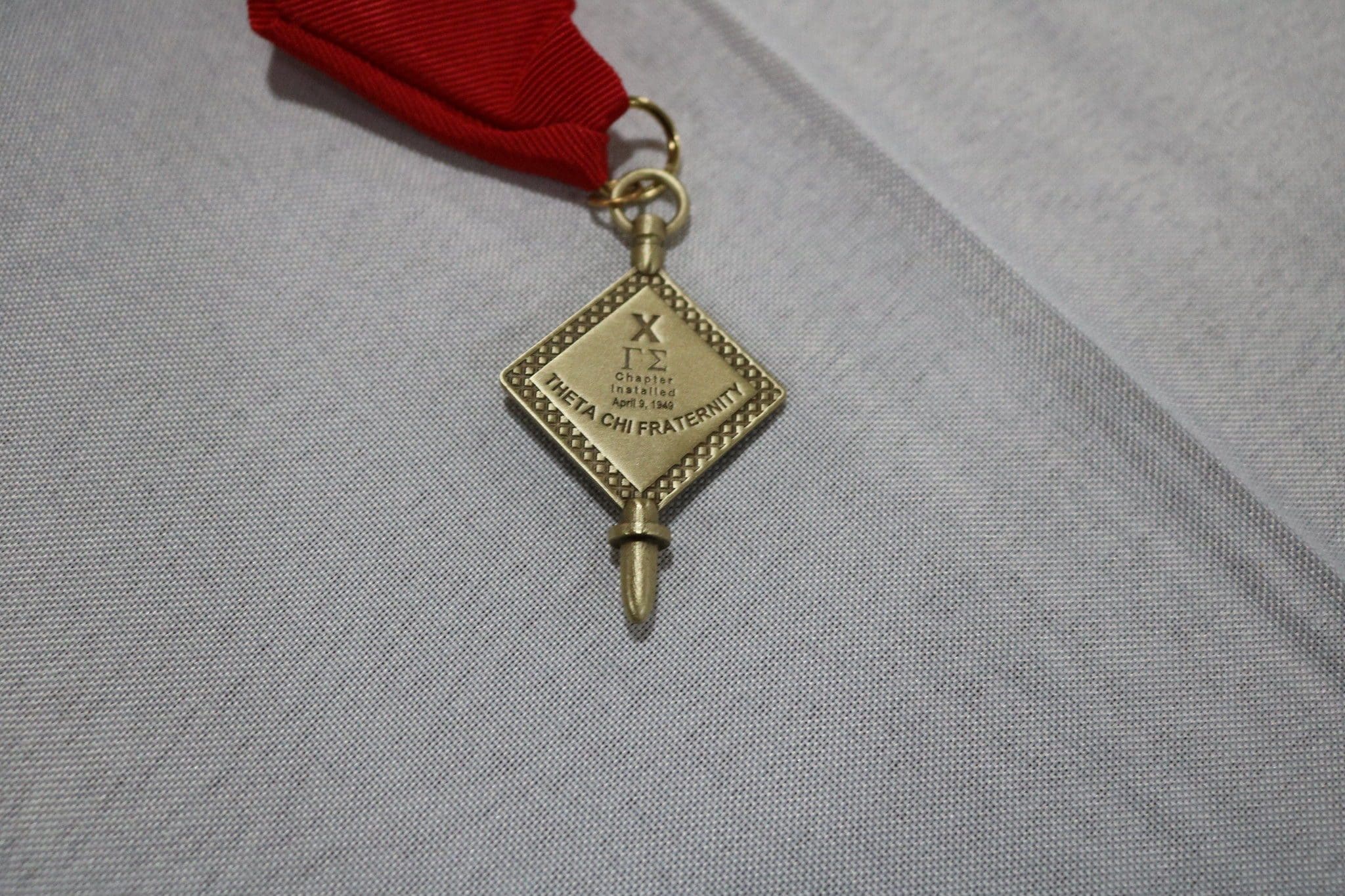 Gold fraternity medal with red ribbon attachment.