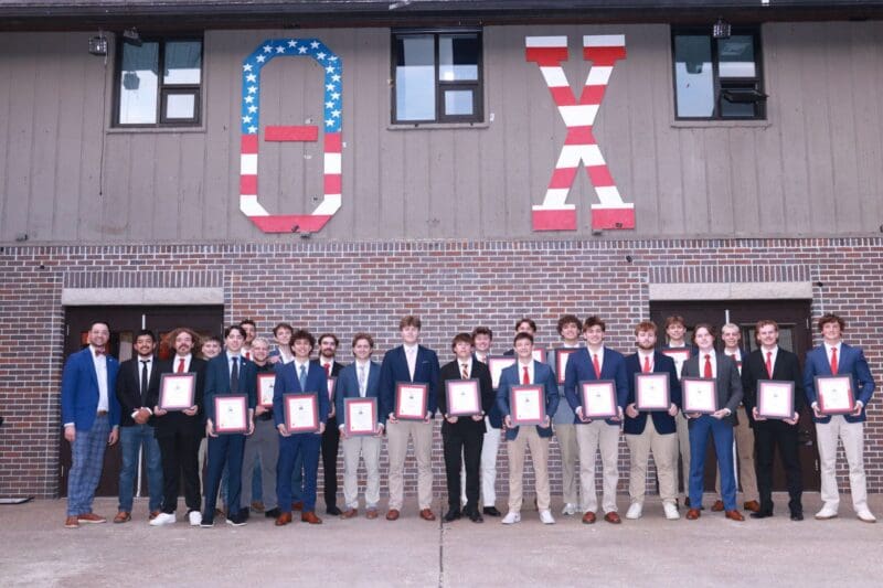 Group of young men holding awards outside building.