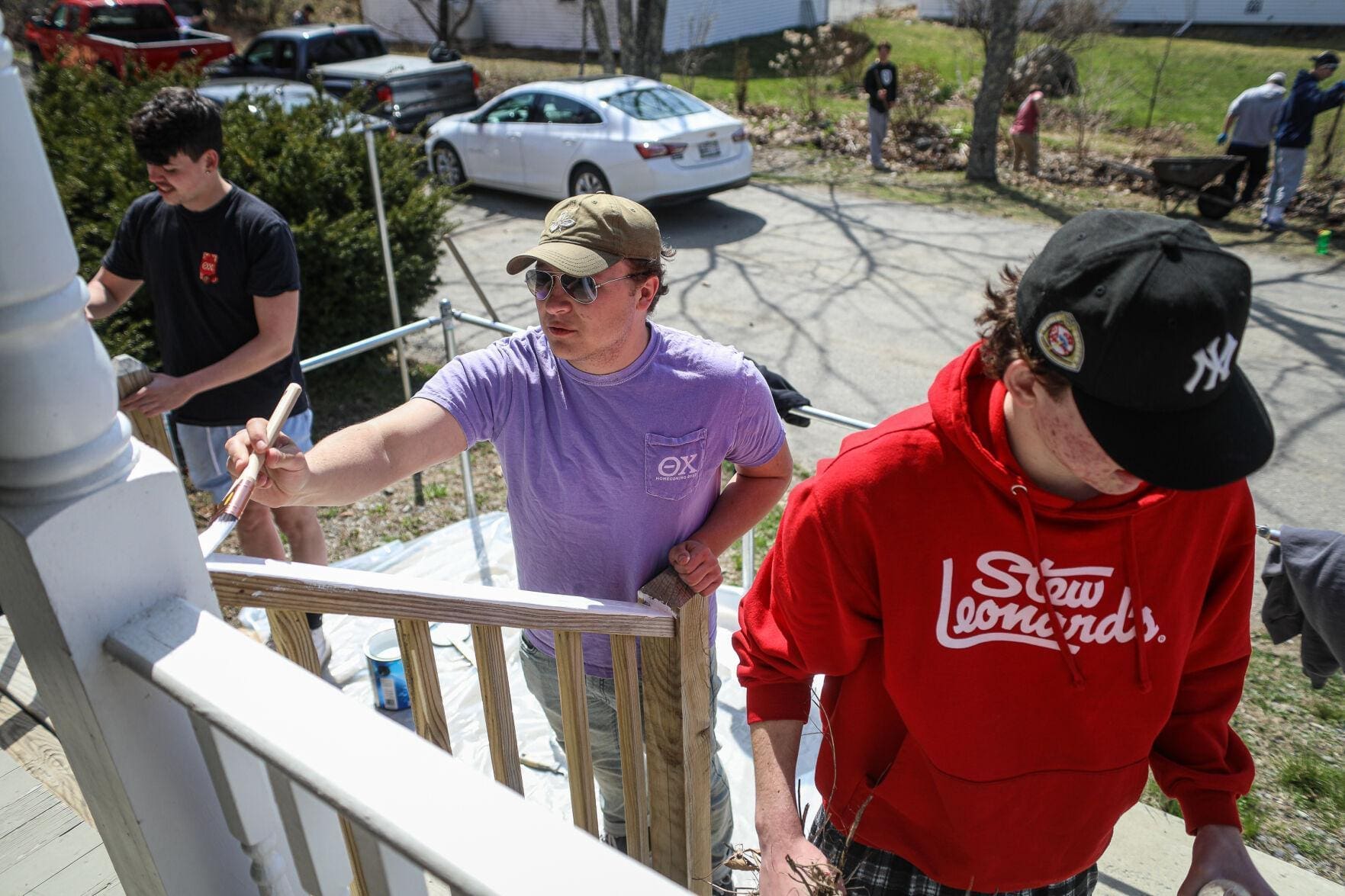 Volunteers painting a wooden railing outdoors on a sunny day.