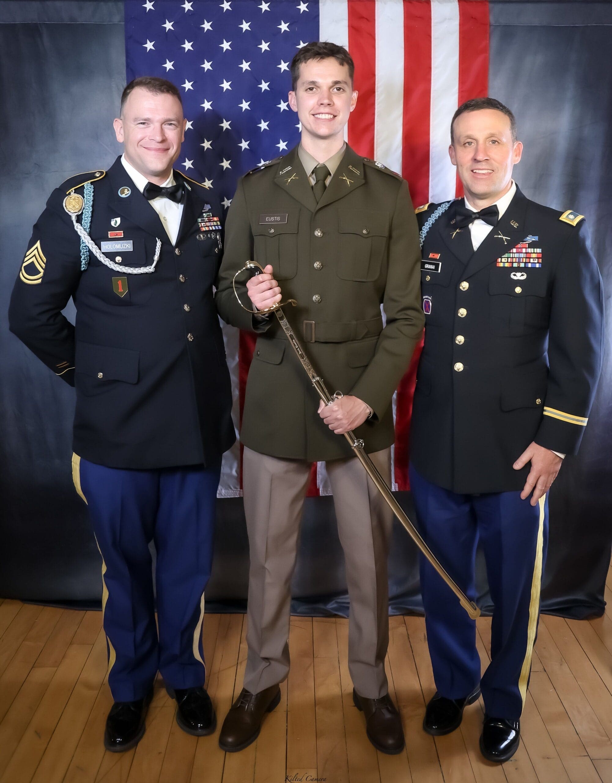 Three military personnel posing with a sword and flag.