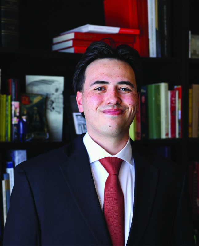Photo of a man in a suit in front of a bookcase