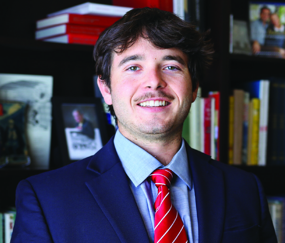 Man in a suit standing in front of a book case.