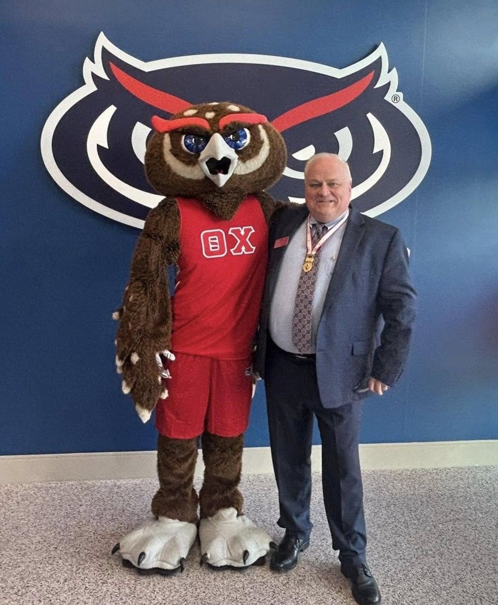Owl mascot with official at university event.