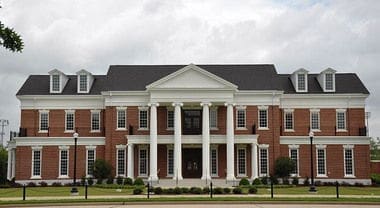 Elegant brick building with columns and landscaped entrance.