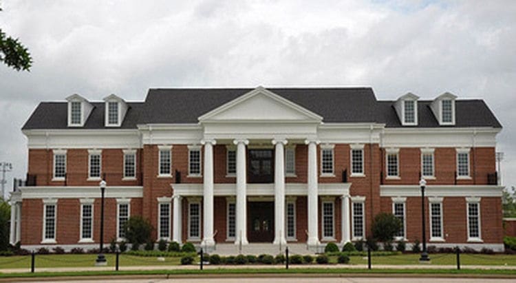 Grand brick mansion with columns and landscaped yard.