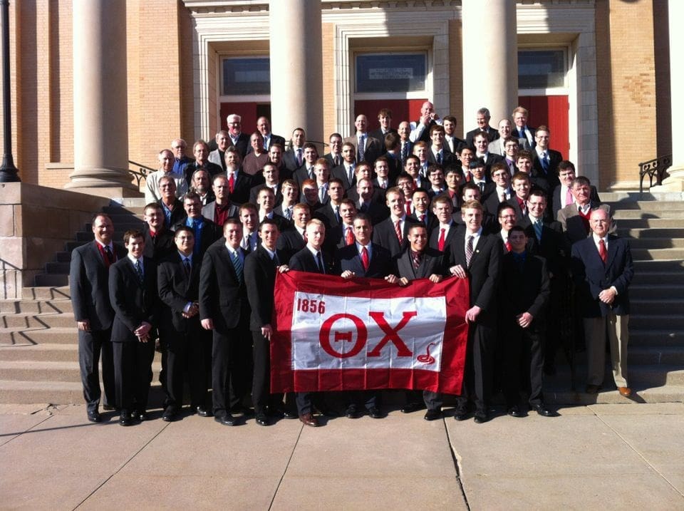 Group of fraternity members posing with flag.