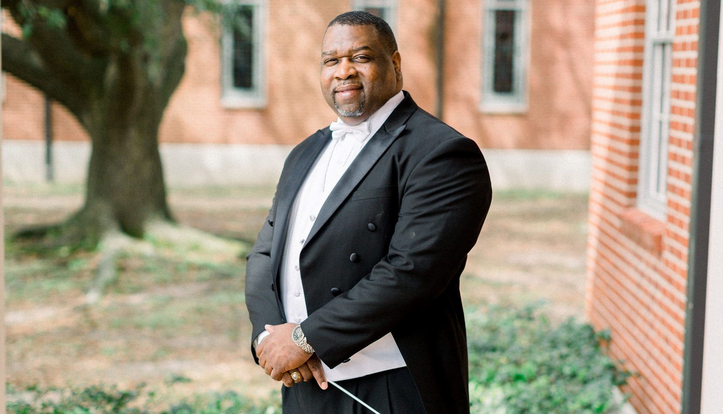 Conductor in formal attire standing outdoors.