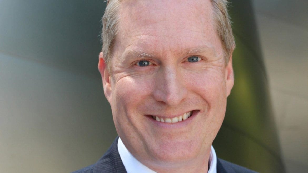 Andrew Brown Smiling man in a business suit outdoors.