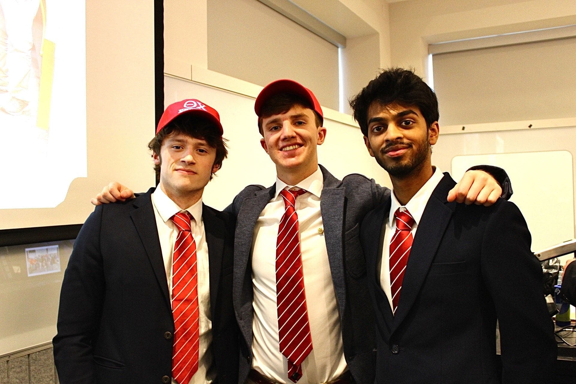 Three friends in suits with red ties and caps.