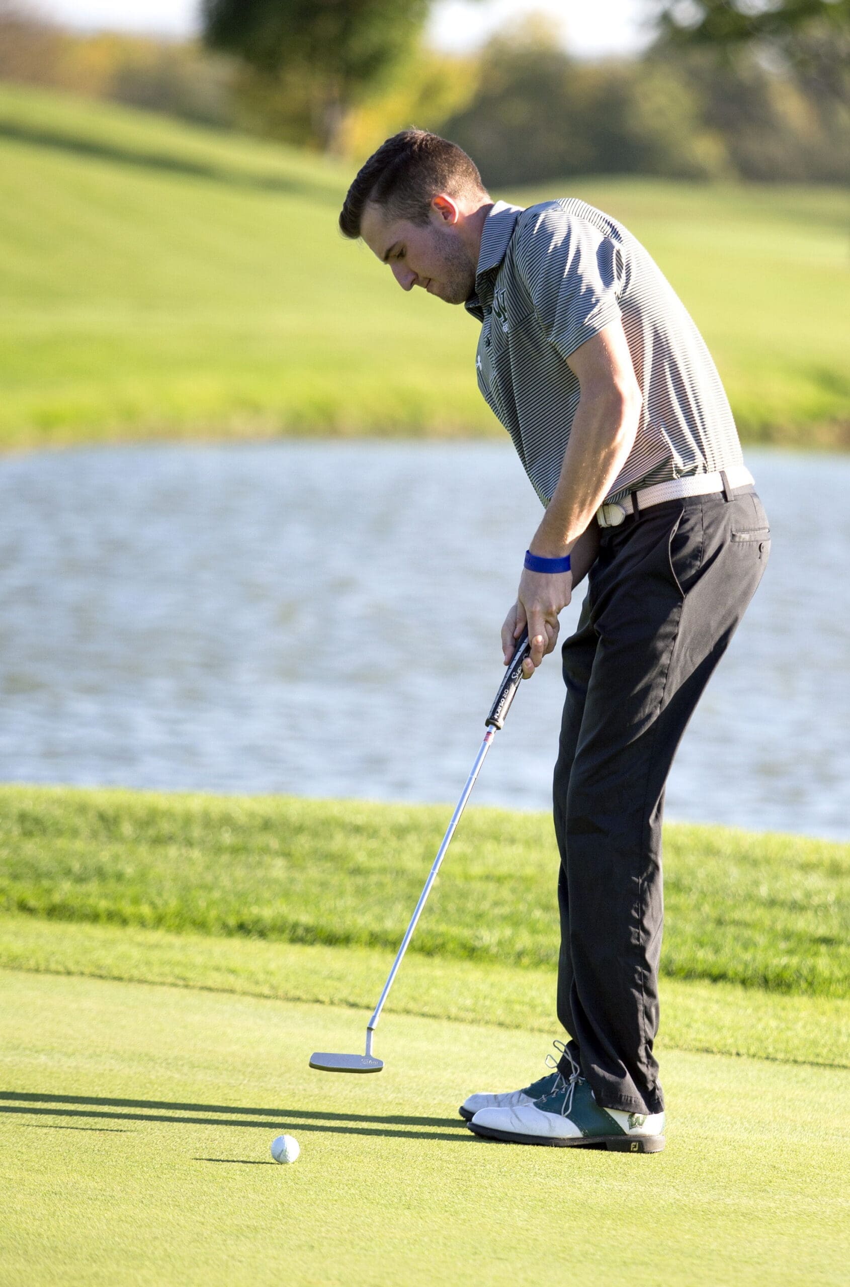 Golfer putting on green near water hazard.