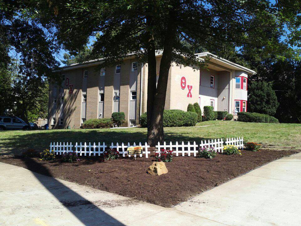 Fraternity house with landscaped garden and white fence.