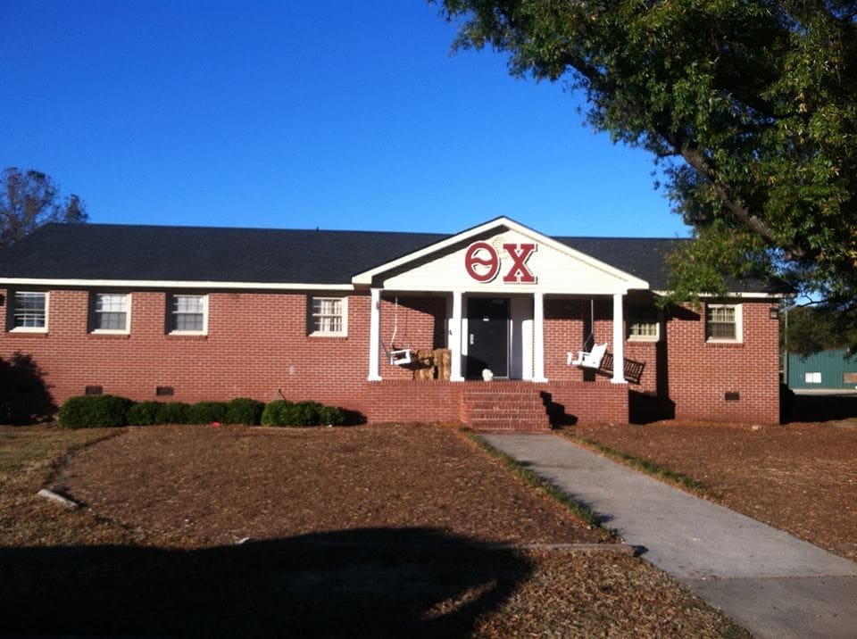 Brick fraternity house with porch and lawn.