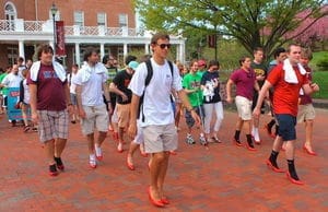 Men walking in red high heels for charity event.
