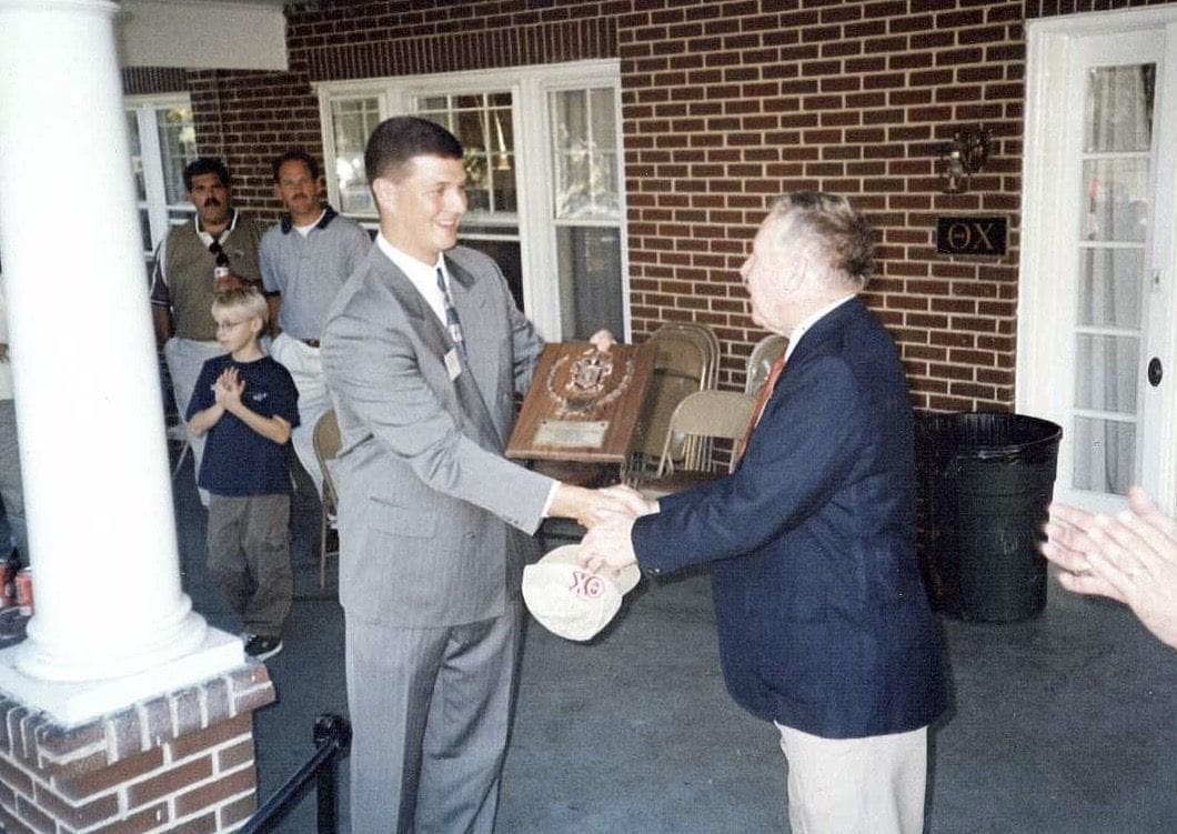 Graham Kenneweg Men exchanging award plaque at a formal event.