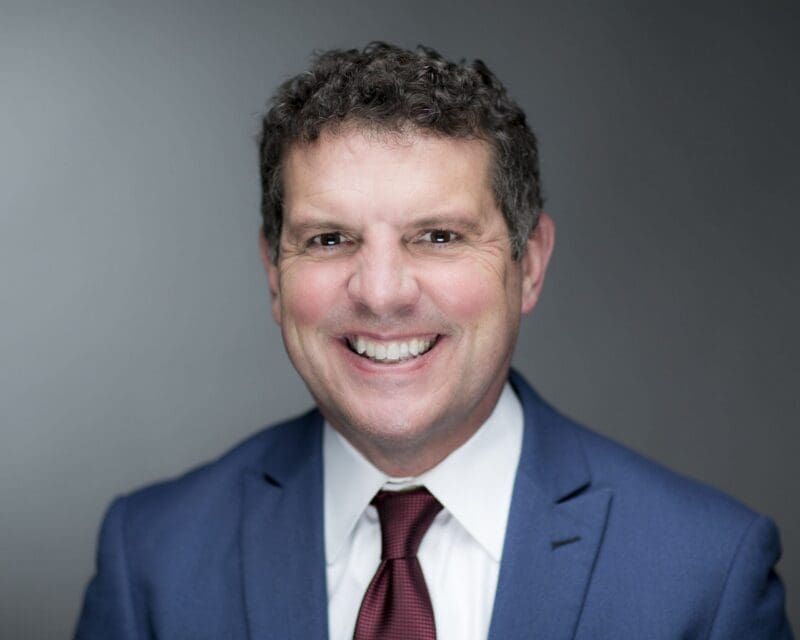 Smiling professional man in a suit against gray backdrop.