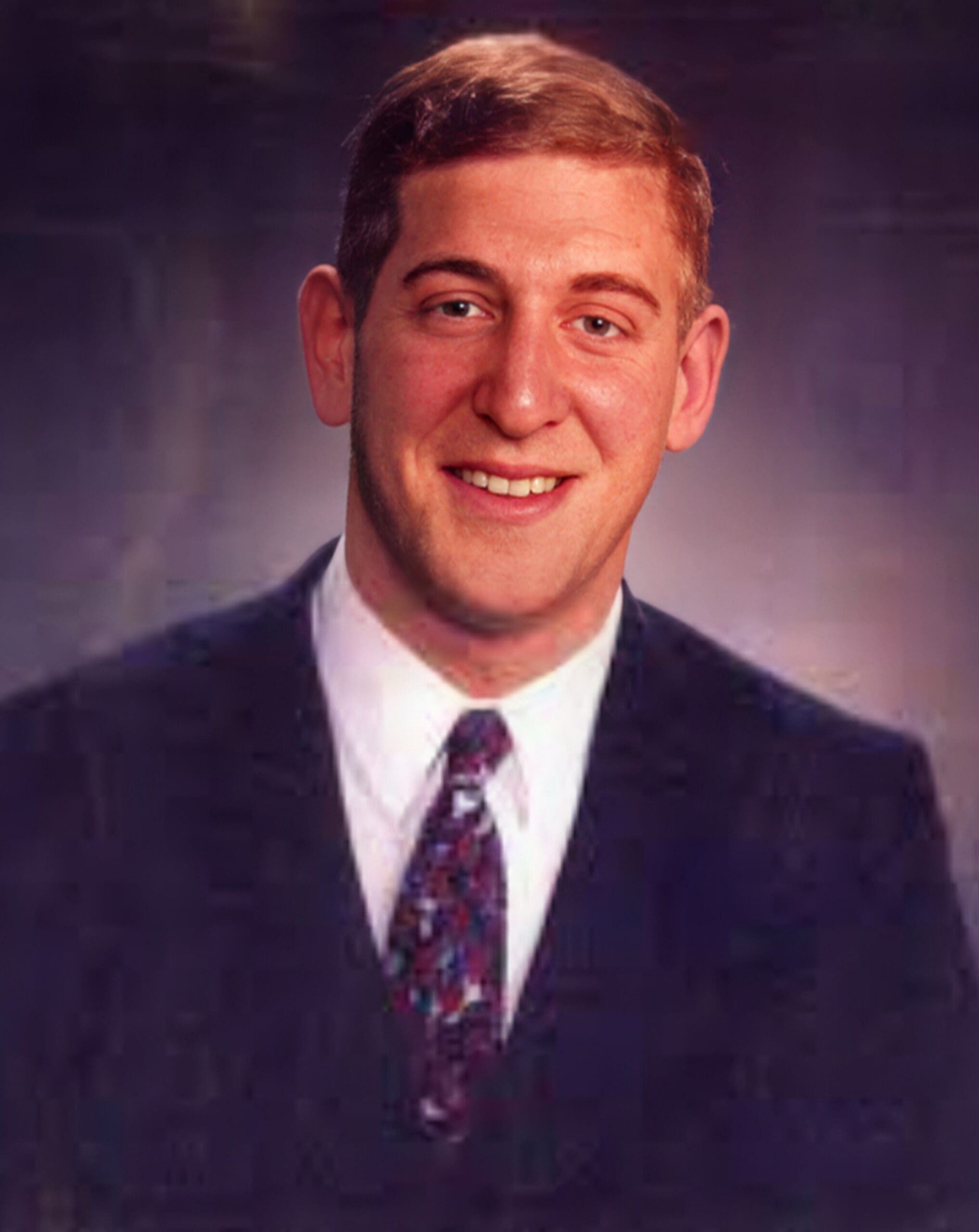 Smiling man in a suit with a patterned tie.