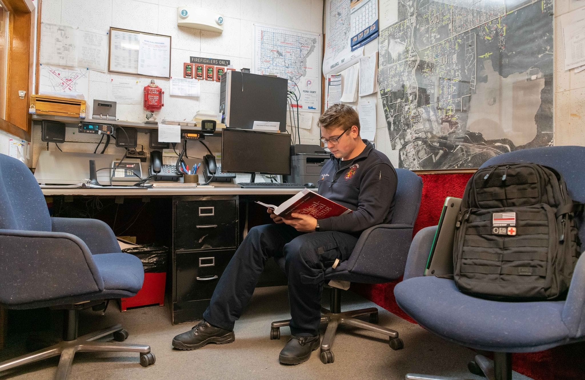 Aaron Coulombe - Bradley Firefighter reading in office with maps and equipment.