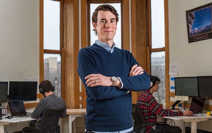 Brock Hensen Young man in sweater standing confidently in office.