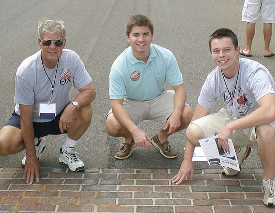 Buddy Davis Three men kneeling beside a brick sidewalk.
