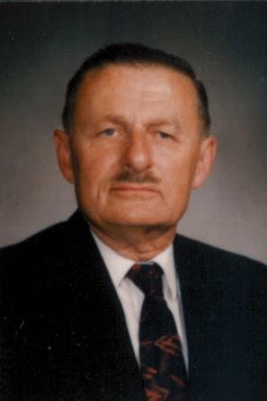 Elderly man in formal attire, serious expression.