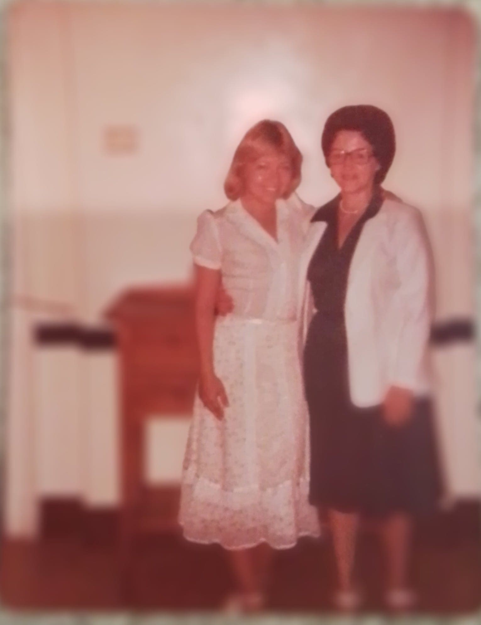 Two women posing together in a softly lit room.