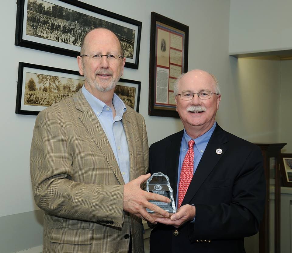 Two men presenting an award in an office setting.