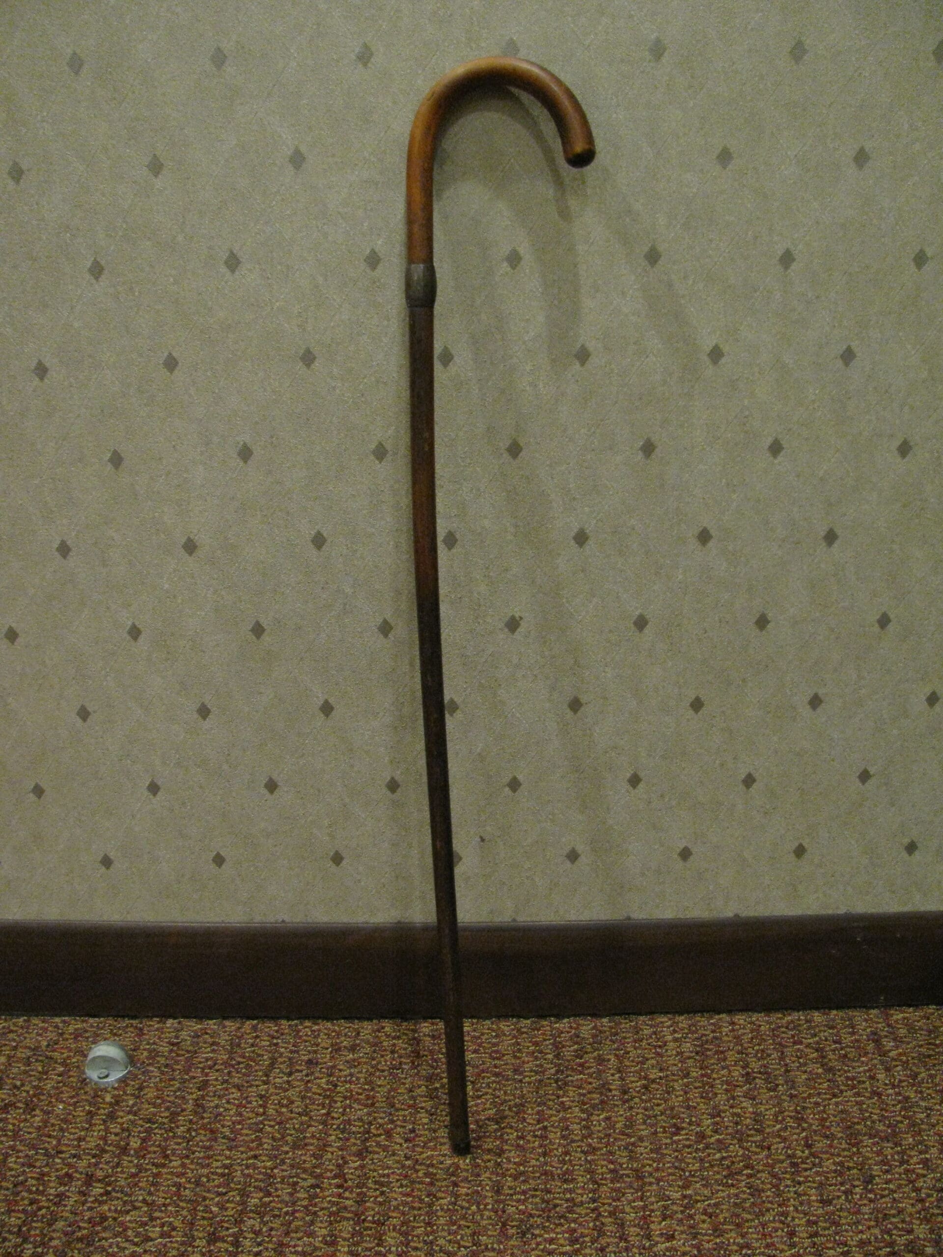 Cane Wooden walking cane against a patterned wall.