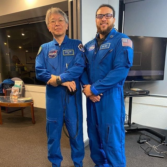 Two astronauts in blue jumpsuits posing together.