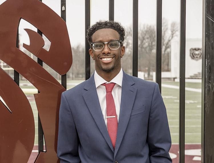 Abdillahi Dirie - Missouri State Smiling man in a suit at a sports field.