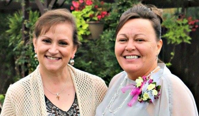 Two smiling women posing outdoors with floral decorations.