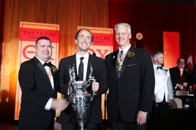 Three men in tuxedos holding a trophy at an event.