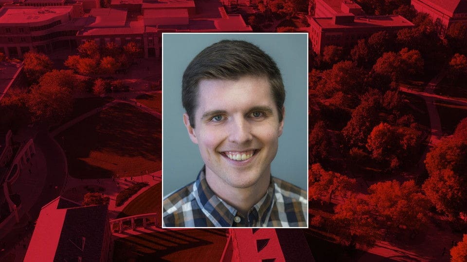 Smiling man in plaid shirt with university background.